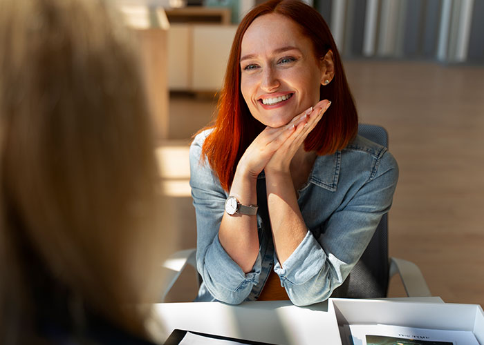 Smiling red-haired woman in denim jacket talking with another person, illustrating men losing interest in a woman.