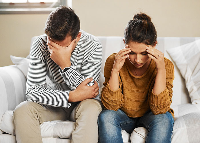 Couple sitting on couch looking upset, illustrating icks that make men lose interest in a woman in relationships.