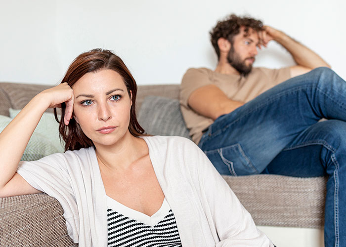 A frustrated woman and man sitting apart on a couch, illustrating men losing interest in a woman.