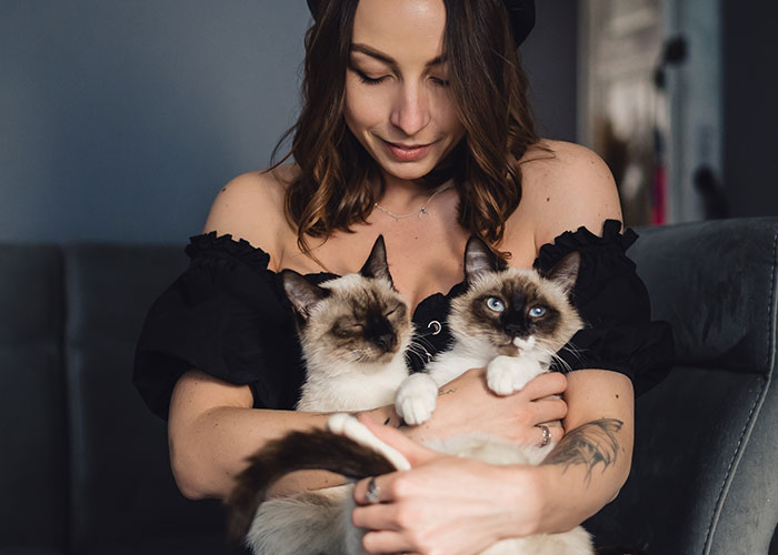 Woman in a black off-shoulder top holding two cats, representing icks that make men lose interest in a woman.