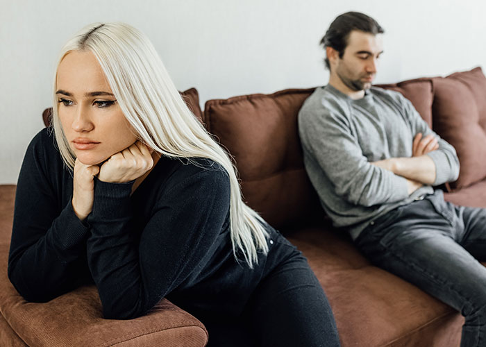 A frustrated woman and man sitting apart on a couch, illustrating icks men notice that make them lose interest in a woman.