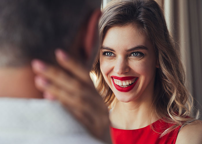 A woman with red lipstick smiling warmly at a man, illustrating common icks that make men lose interest in a woman.
