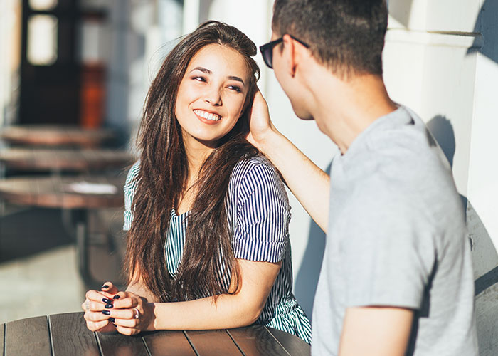 A man gently touching a smiling woman’s hair outdoors, illustrating common icks that make men lose interest in a woman.