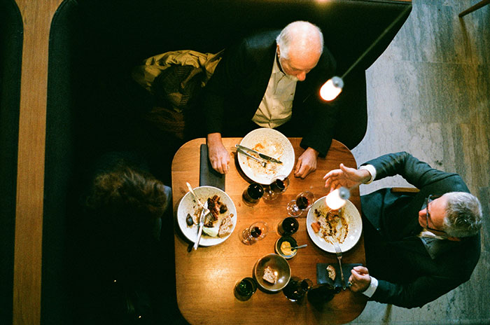 Overhead view of three adults dining at a table, illustrating Bulgarian finds out the Dutch don’t share food. Overhead view of three adults dining at a table, illustrating Bulgarian finds out the Dutch don’t share food.
