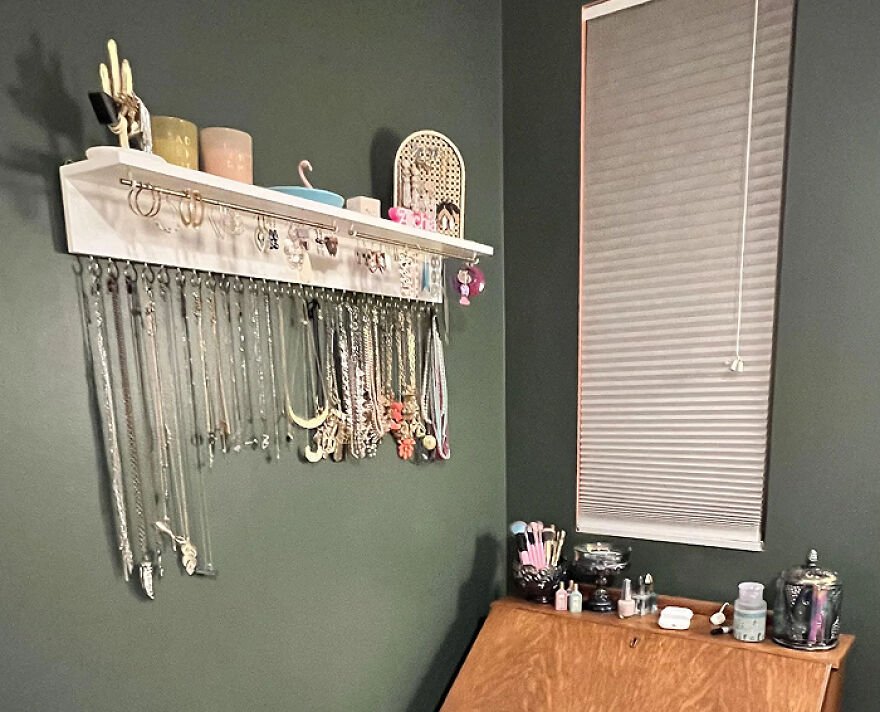 Jewelry hanging neatly on wall hooks and organized makeup items on a wooden desk in a tidy home space.