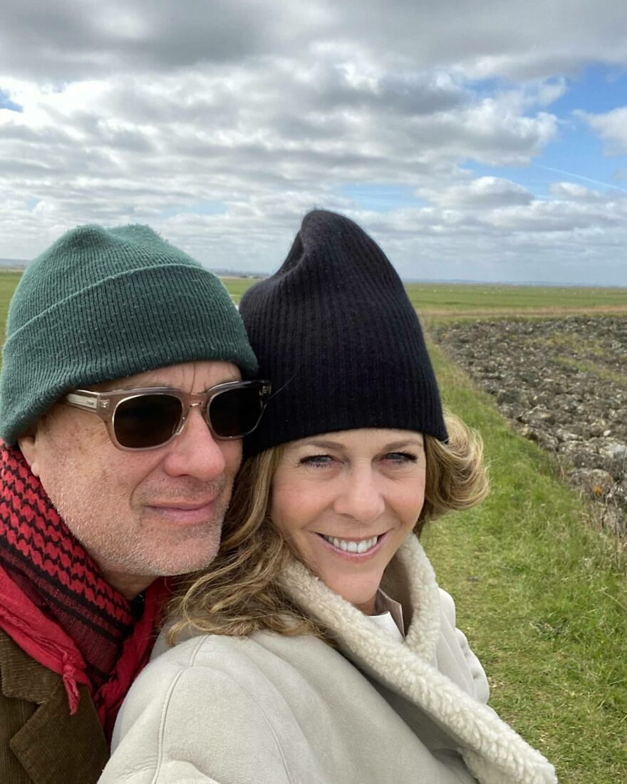 Tom Hanks And Rita Wilson wearing winter hats outdoors, smiling and enjoying a scenic landscape, showing Hollywood power couples together.