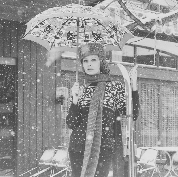 Sophia Loren standing in snow with umbrella and skis, showcasing Italian beauty and Hollywood legend style.