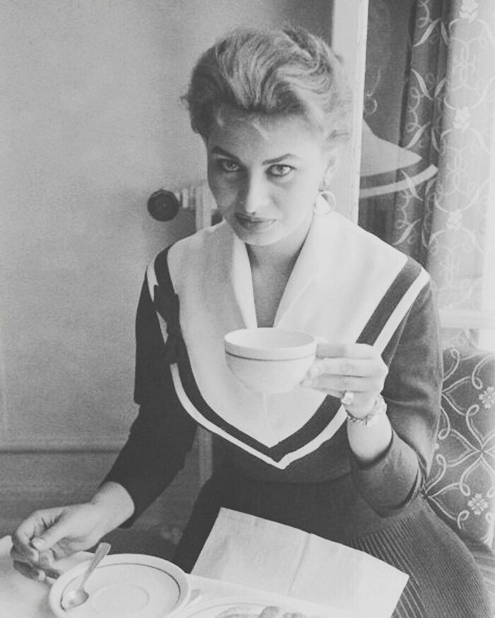 Sophia Loren sitting indoors holding a teacup, showcasing Italian beauty and classic Hollywood elegance in black and white.