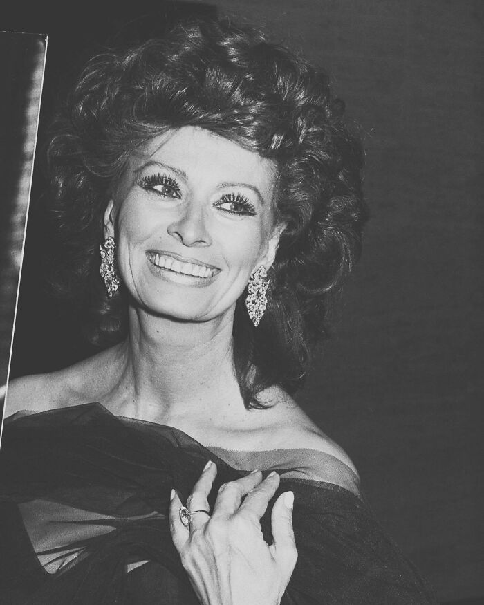 Sophia Loren smiling in elegant attire with large earrings, showcasing Italian beauty and Hollywood legend charisma in black and white.