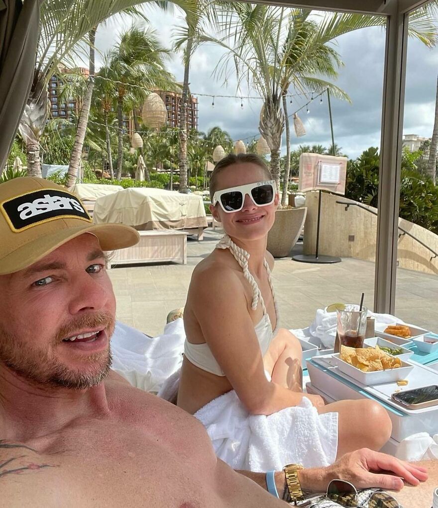 Kristen Bell And Dax Shepard relaxing poolside at a tropical resort, enjoying food and drinks, representing Hollywood’s enduring power couples.