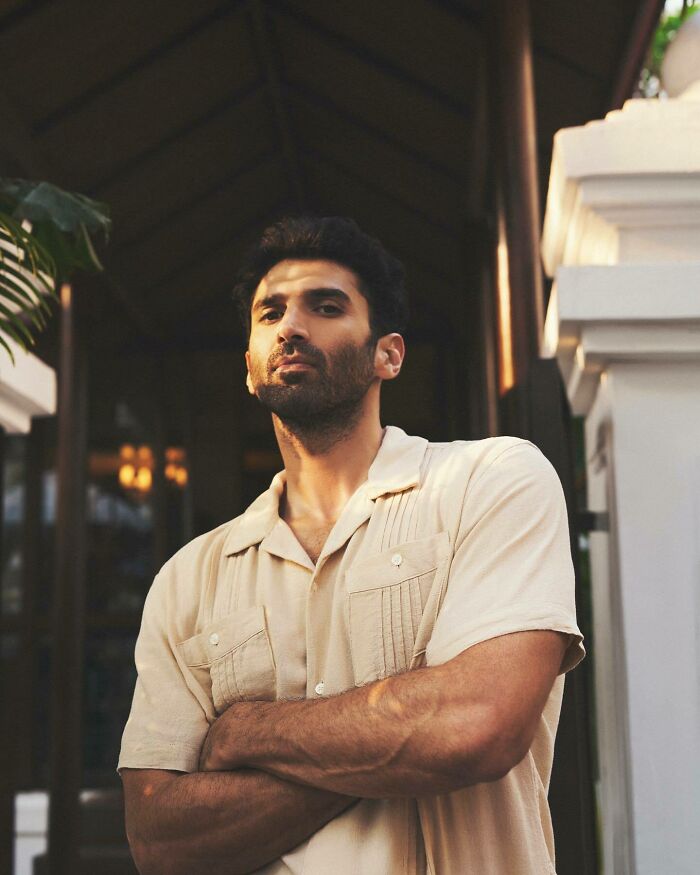 Man with beard and short dark hair wearing a beige shirt posing confidently as most handsome man in the world 2025.