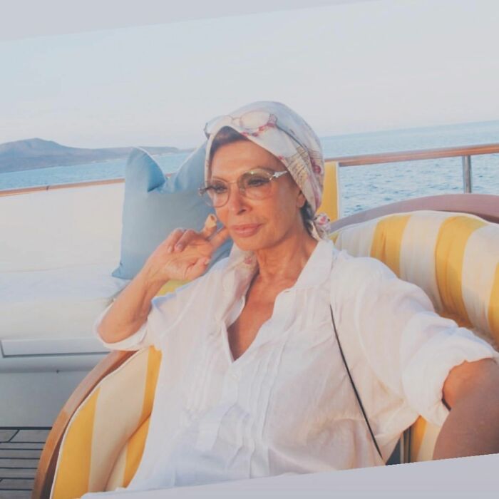 Sophia Loren relaxing on a boat, wearing glasses and a headscarf, showcasing timeless Italian beauty and Hollywood elegance.