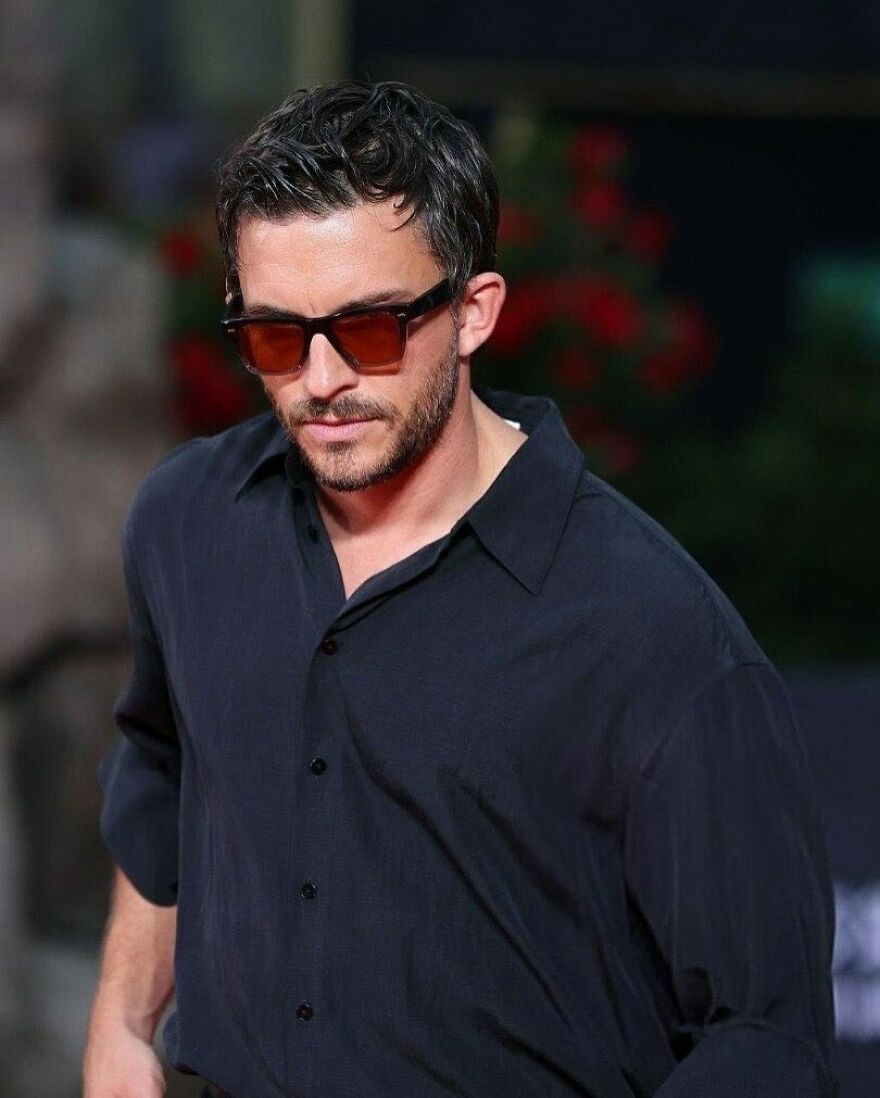 Jonathan Bailey wearing sunglasses and a black shirt, styled hair, representing most handsome man in the world 2025.