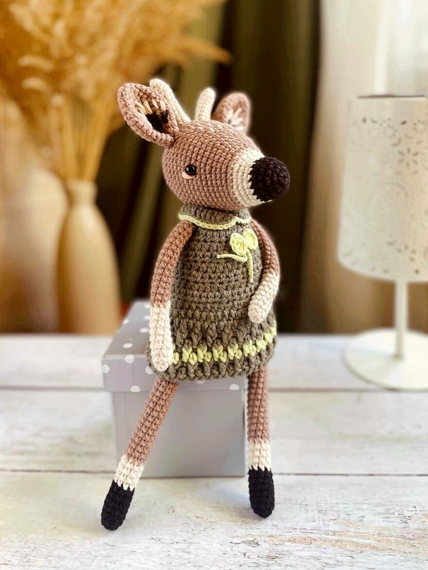 Crochet animal doll with personality, sitting on a box, featuring detailed stitching and soft colors in a cozy setting.