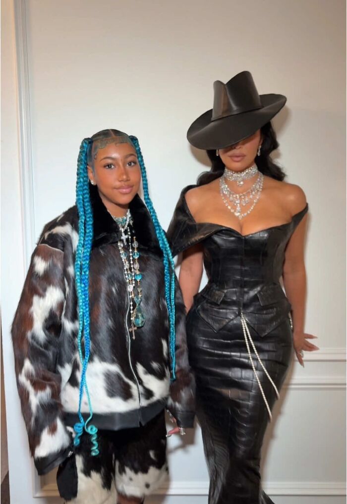 North West with blue braids and stylish outfit, wearing fake face tattoos, piercings, and grills, sparking concern.