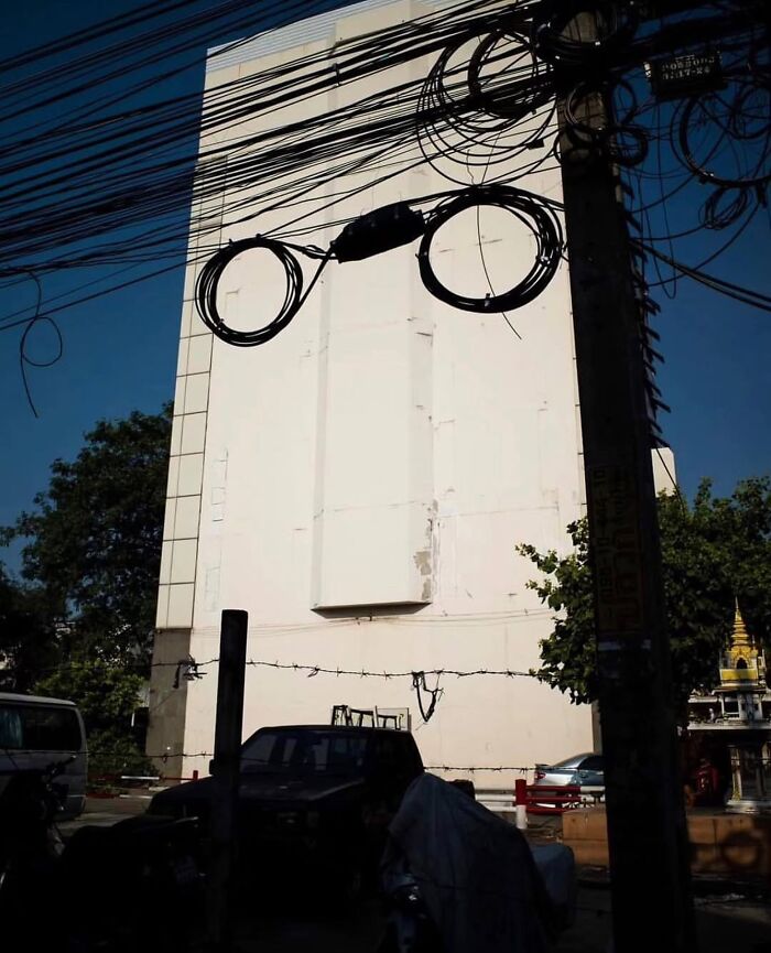 Coiled cables on utility pole create the appearance of glasses against a white building in a fascinating photo.