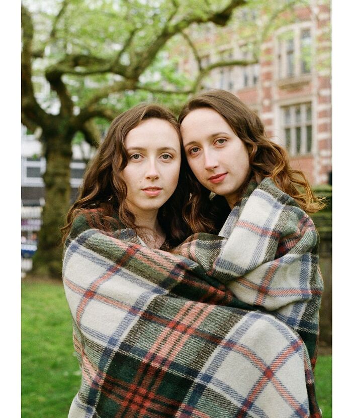 Twin sisters wrapped in a plaid blanket outdoors, captured by a London photographer showcasing their unique bond.
