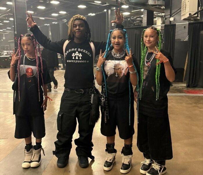 Four young people posing indoors with colorful braids, showcasing fake face tattoos, piercings, and grills fashion.