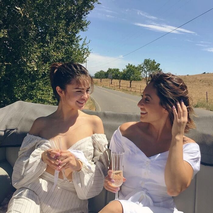Two women smiling and holding champagne flutes outdoors on a sunny day, fans curious about Selena Gomez kidney donor.