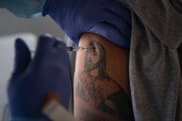 Close-up of a person receiving a vaccine shot with a gloved hand near a tattoo in the most fascinating photos collection.