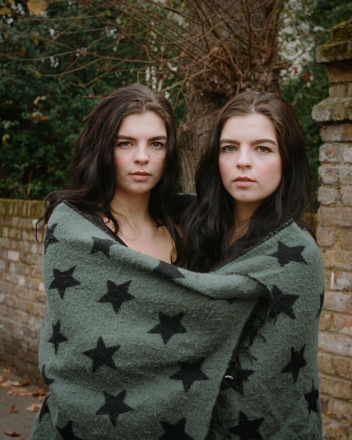 Twin sisters wrapped together in a star-patterned blanket outdoors, captured by a London photographer in an intimate portrait.