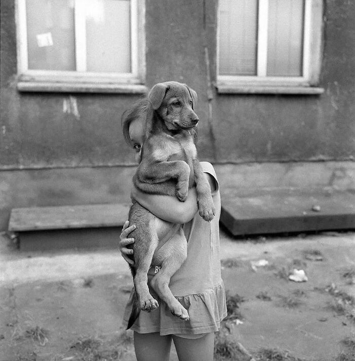 Child holding a puppy in front of a building, captured in one of the most fascinating photos from the newest 30 collection.