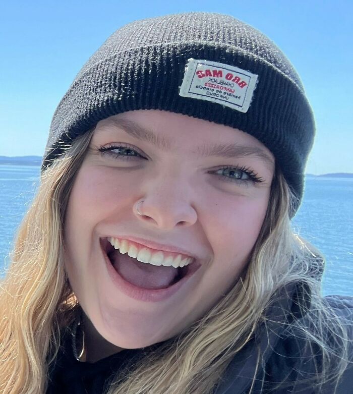 Young woman smiling wearing a black beanie near water, related to music festival accident involving Post Malone.
