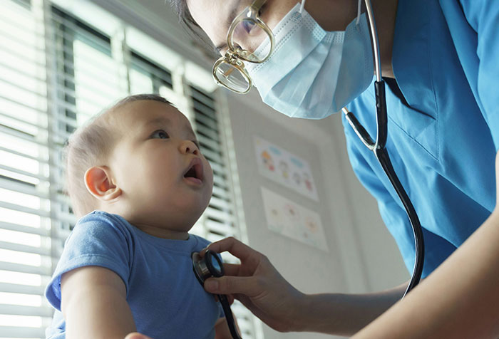 Doctor wearing mask uses stethoscope to examine baby, illustrating cases of people self-diagnosing correctly.
