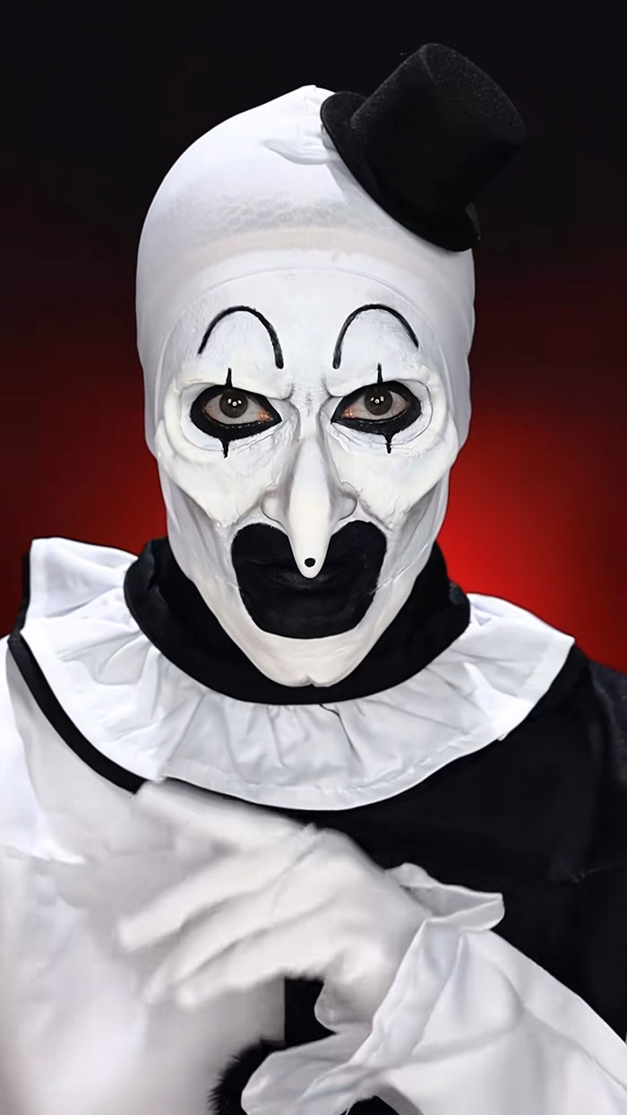 Halloween makeup featuring a black and white creepy clown look with a small top hat on a red background.