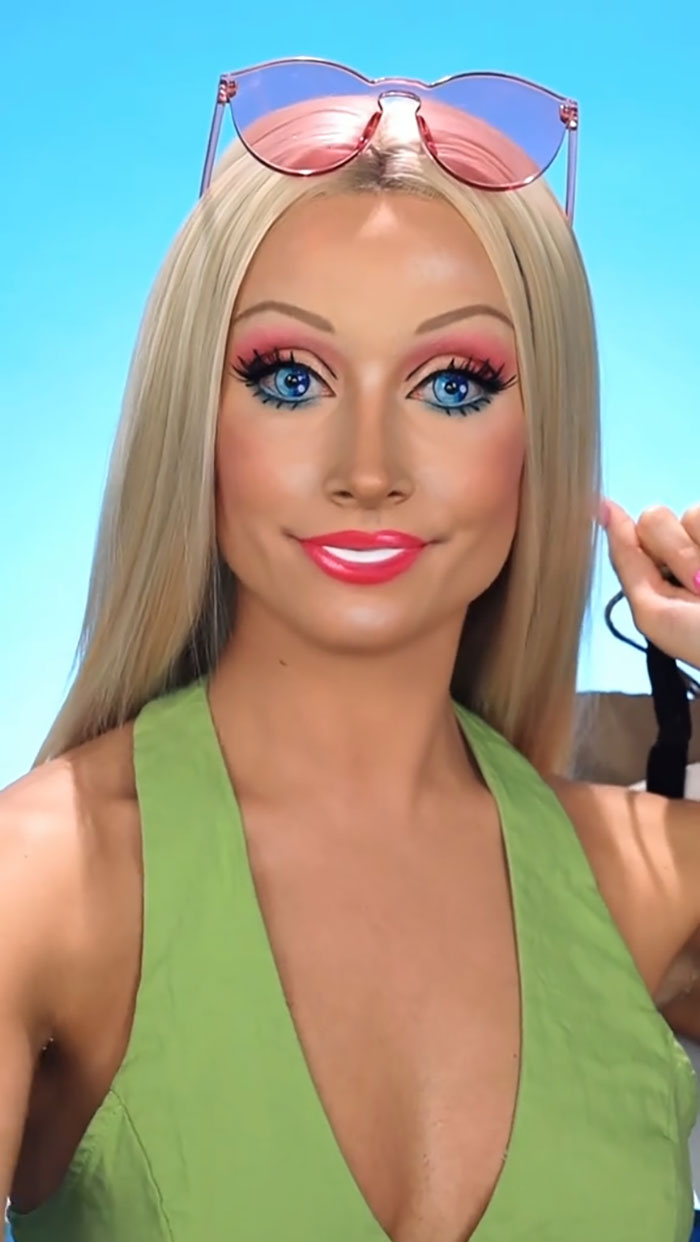 Creative makeup artist with detailed Halloween makeup, wearing green top and pink sunglasses, showcasing artistic skills.