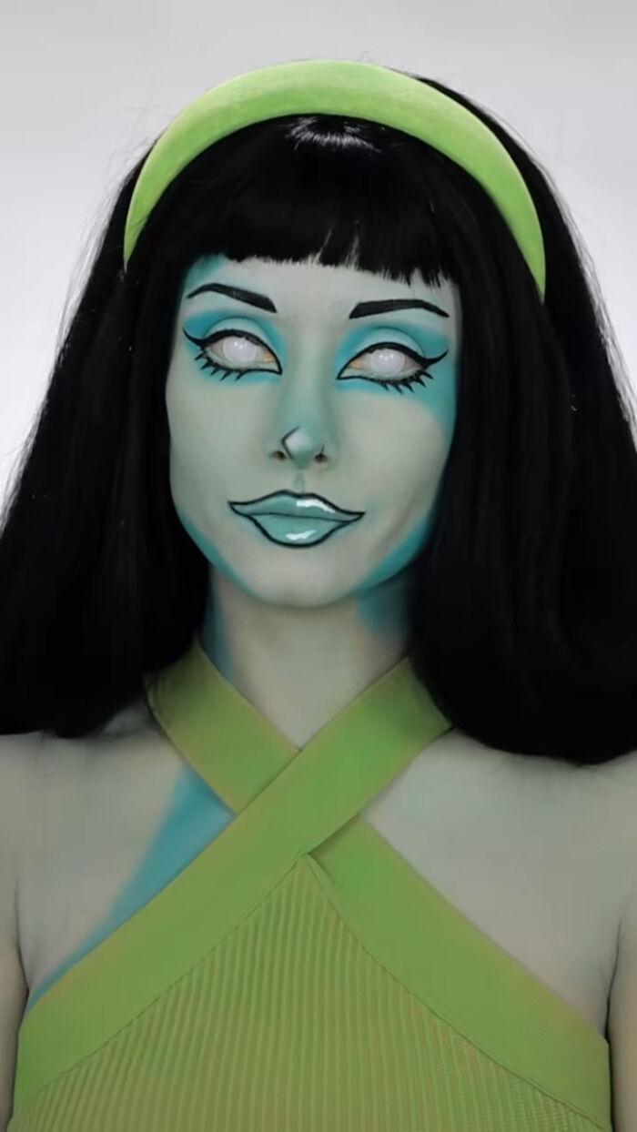 Halloween makeup artist Creative Cliche with intricate green and blue face paint and artistic eye and lip details.