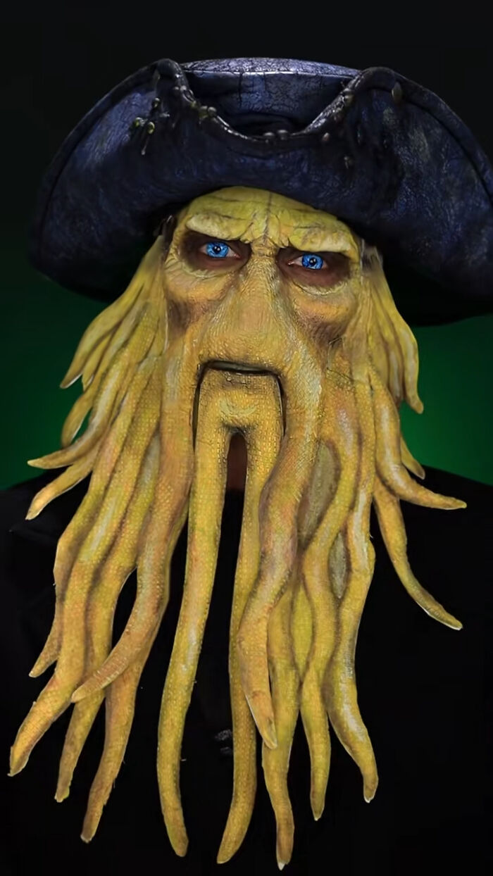 Halloween makeup of a pirate with detailed yellow tentacle beard and bright blue eyes on a dark background.
