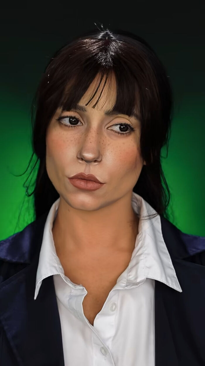 Young woman with detailed Halloween makeup by Creator Creative Cliche, wearing a white shirt and dark jacket against a green background