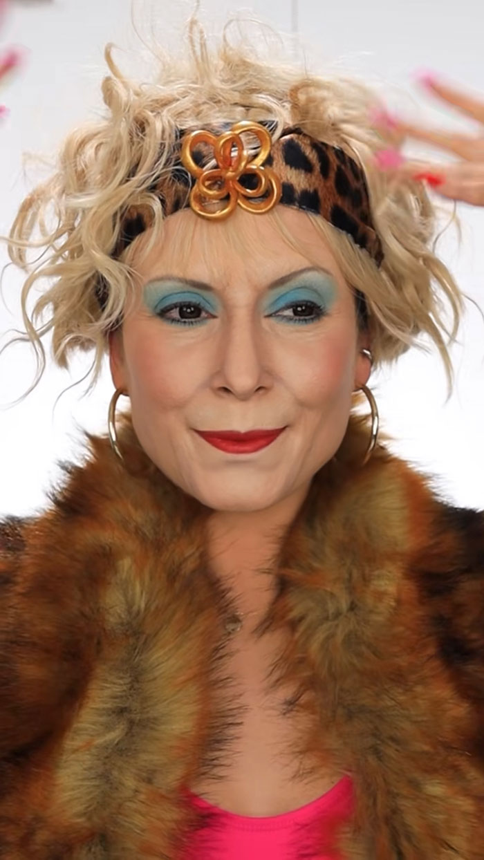 Woman wearing Halloween makeup with blue eyeshadow, red lipstick, leopard headband, and fur coat showcasing creative makeup looks.