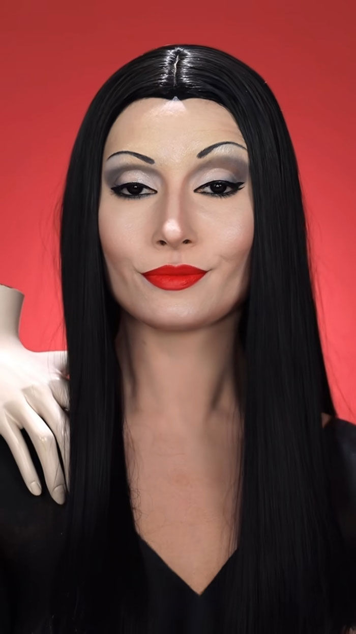Creative Cliche Halloween makeup featuring long black hair, red lips, and dramatic eye makeup on a red background.