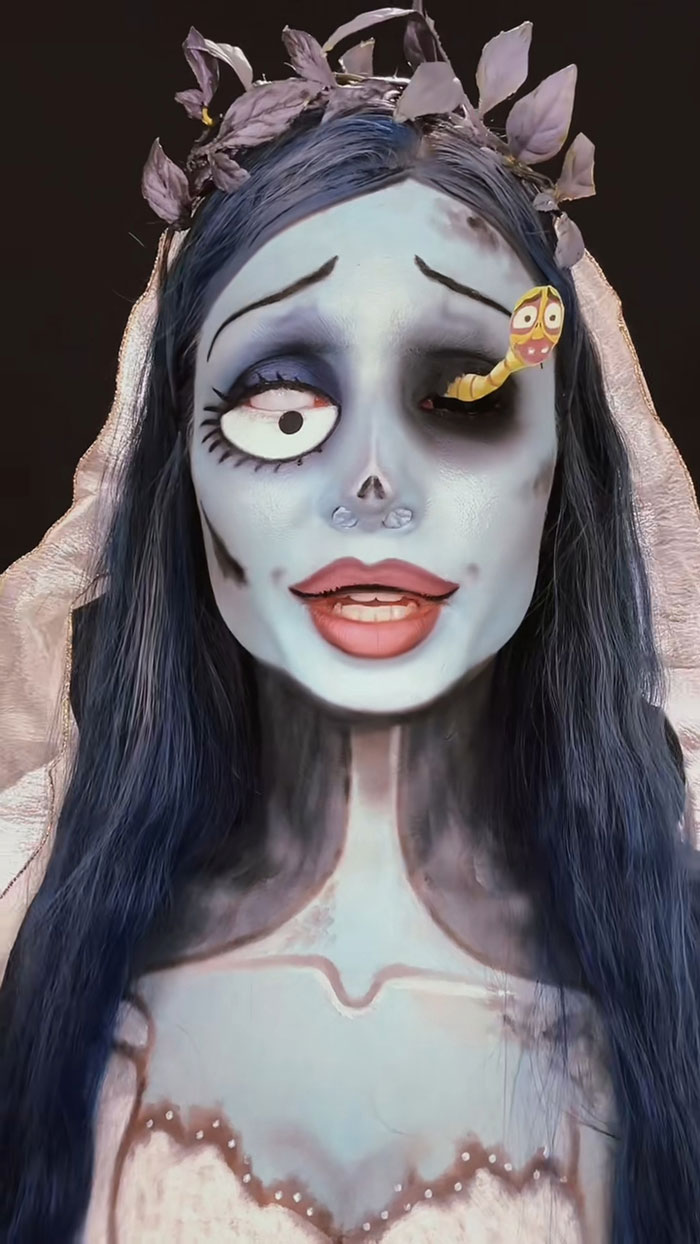 Halloween makeup featuring detailed blue face paint, animated eye effects, and dark floral headpiece by a creative artist.