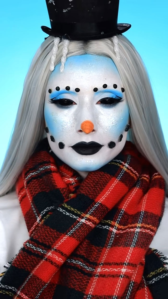 Creative Cliche Halloween makeup featuring a snowman face with white paint, black dots, orange nose, and red plaid scarf.