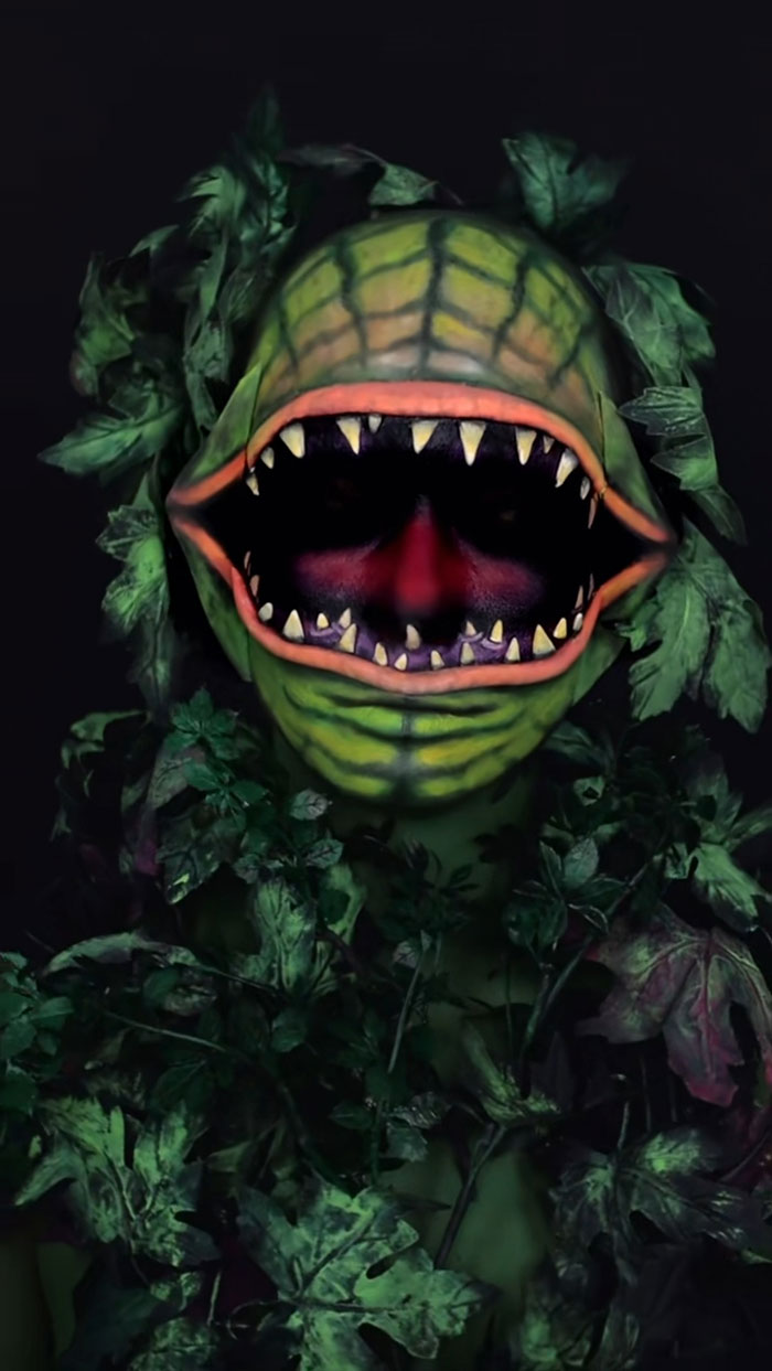 Halloween makeup of a carnivorous plant creature with sharp teeth and green leaves surrounding the face and body.