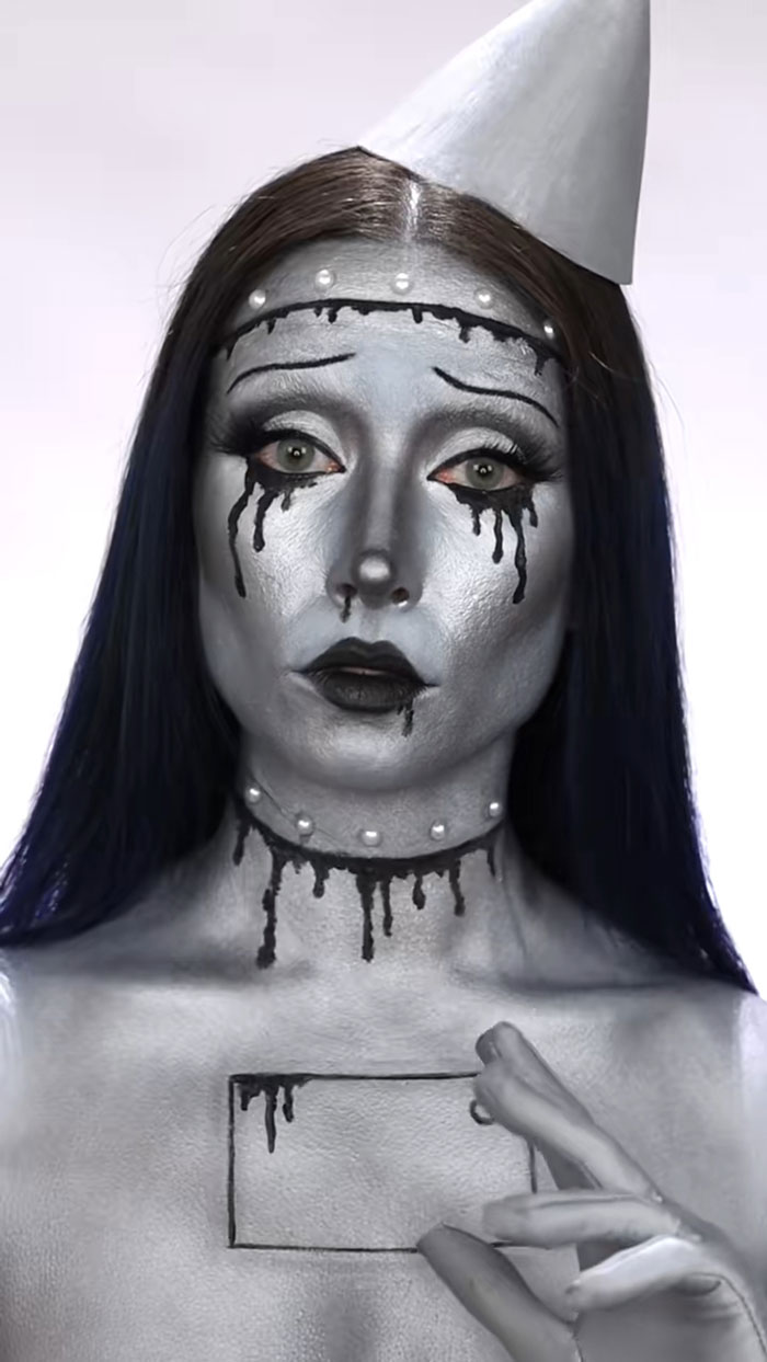 Woman with creative Halloween makeup wearing silver face paint and black dripping details, showcasing artistic Halloween makeup skills.