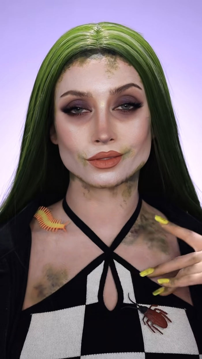 Woman with green hair wearing Halloween makeup featuring creepy bugs and dark eyeshadow for creative Halloween makeup look.