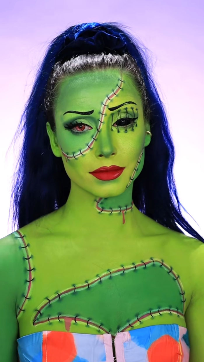 Creative Halloween makeup on a woman with green stitched skin and vibrant red lips against a purple background.