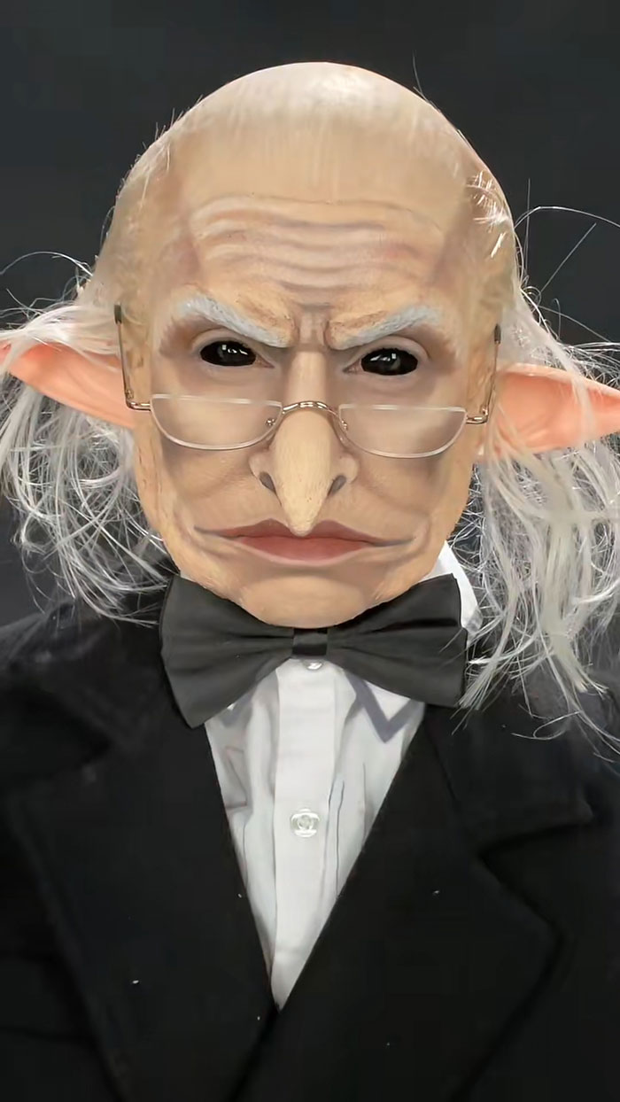 Close-up of creative Halloween makeup showing an old character with large nose, glasses, and pointed ears in formal attire.
