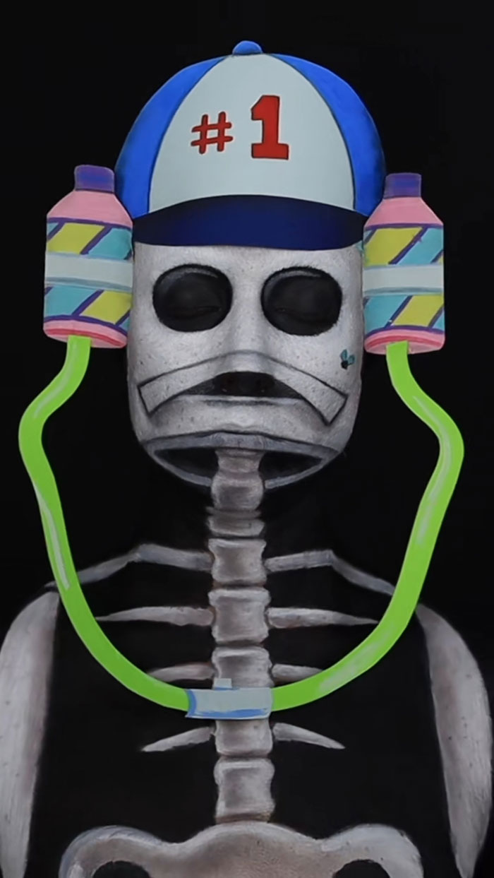 Creative Cliche Halloween makeup featuring a skeleton face with a colorful hat and attached drink holders on a black background.