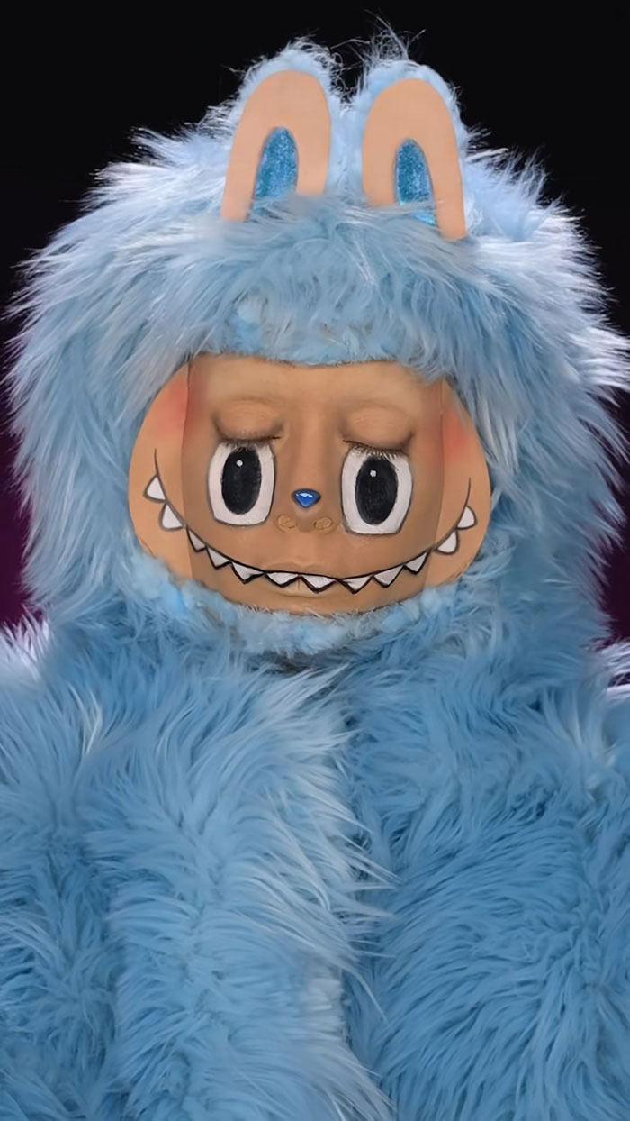 Person with creative Halloween makeup and blue furry costume resembling a cartoon monster by Creator Creative Cliche.