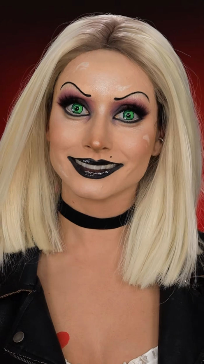Woman with amazing Halloween makeup featuring green eyes, black lips, and dramatic eye shadow and eyeliner on a red background.