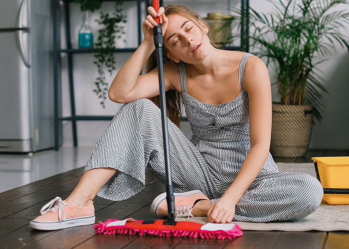 Young woman exhausted from cleaning, sitting on floor with mop, reflecting stress of being treated like a maid by in-laws.