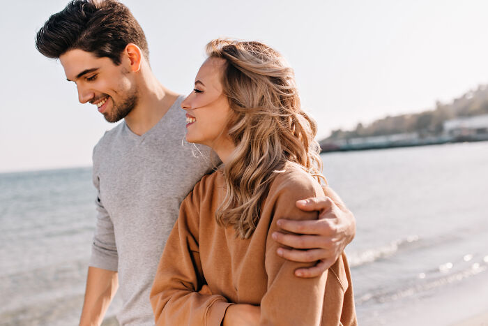 Young couple smiling and walking by the beach, enjoying life and discovering 24 loopholes to take advantage of today.