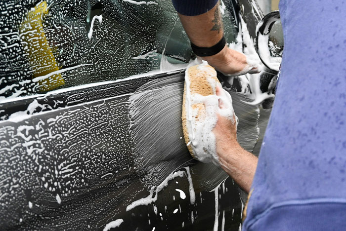 Person washing a soapy black car with a sponge, illustrating instant karma moments in everyday life.