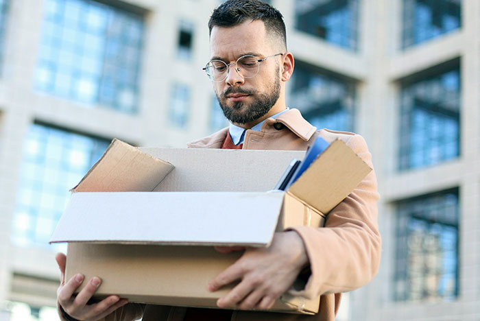 Man with glasses holding cardboard boxes outside an office building, symbolizing instant karma moments in life.