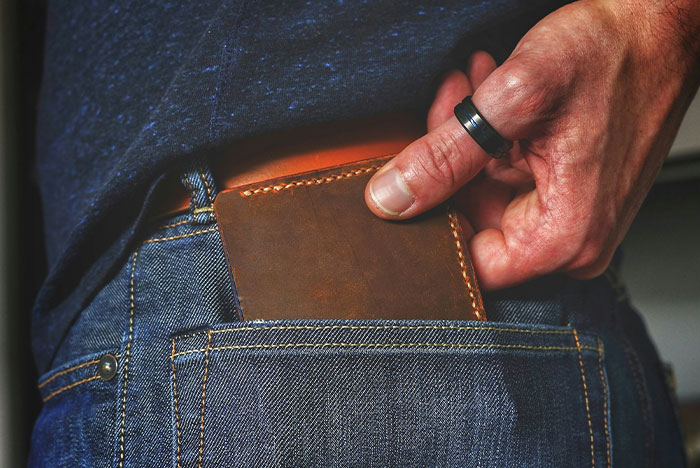 Close-up of a person retrieving a brown leather wallet from a back pocket illustrating instant karma concept.